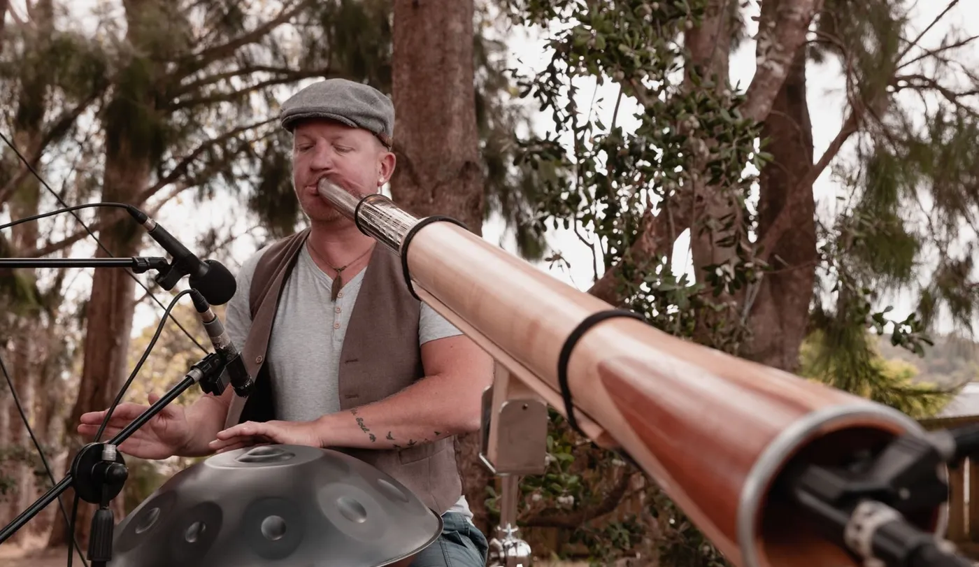 Chewy playing the didgeridoo alongside a handpan in an outdoor setting